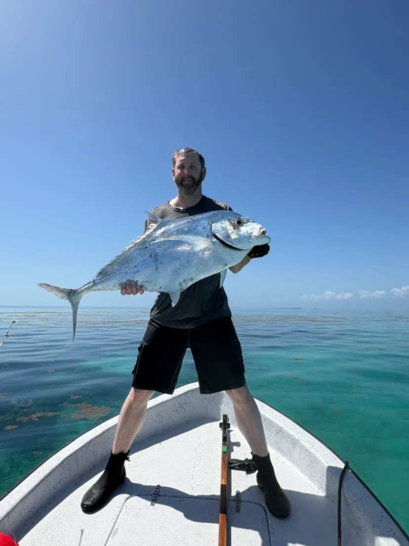 Angler on the bow holding a big jack over turquoise water