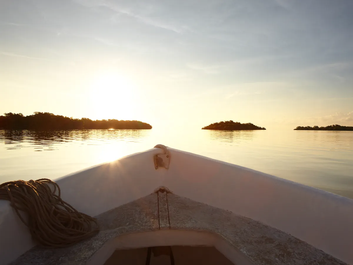 Boat bow on calm water at sunset with cayes on the horizon